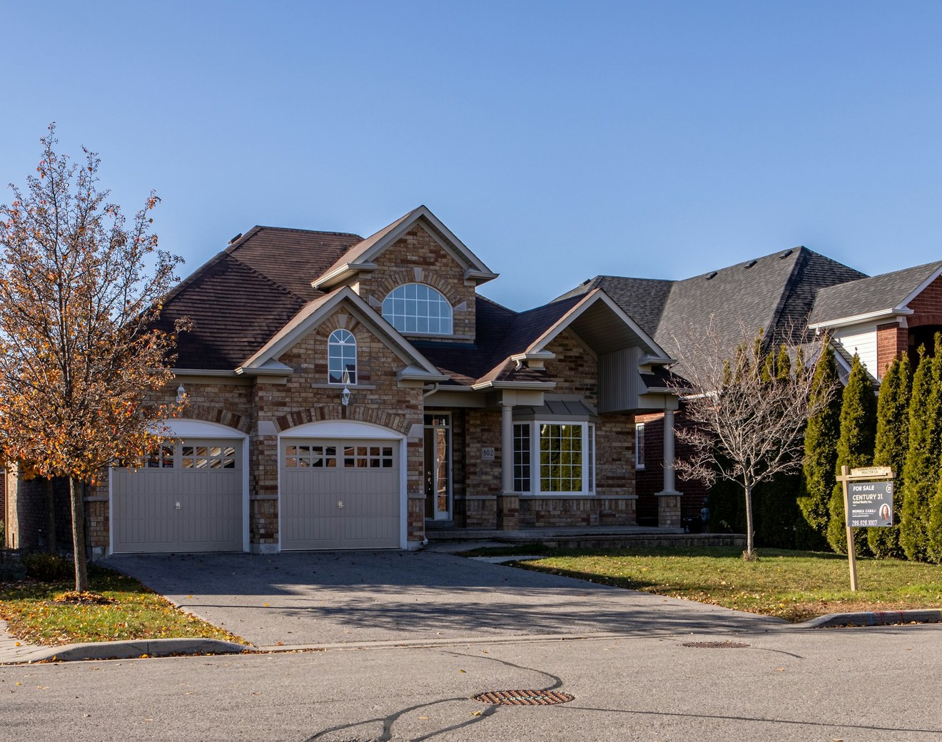 Brick two-story suburban home with a two-car garage and a For Sale sign on the front lawn